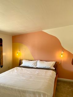 a bed with white sheets and pillows in a room that has an orange accent on the wall