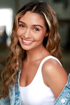 a beautiful young woman with long curly hair wearing a white tank top and jean jacket