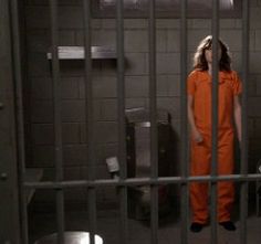 a woman in an orange jumpsuit is standing behind bars inside a jail cell area