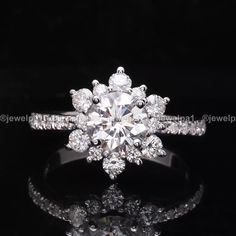 an engagement ring with a flower shaped center surrounded by round brilliant cut diamonds on a black background