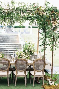 an outdoor dining table with chairs and greenery on the top is surrounded by white flowers