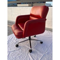 a red leather office chair sitting on top of a white sheet covered floor next to a building