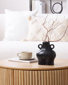 a black vase sitting on top of a wooden table next to a cup and saucer