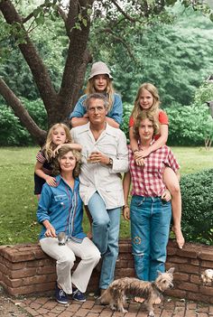 a family poses for a photo in front of a tree and brick wall with their dog