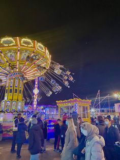 people are standing around in front of a merry go round at the fairground with lights on