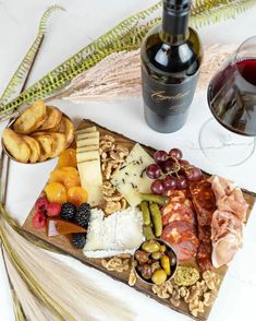 a wine bottle and some snacks on a wooden platter next to a glass of red wine