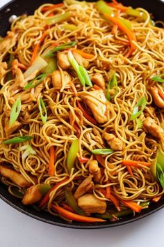 a pan filled with noodles and vegetables on top of a white countertop next to a wooden spoon