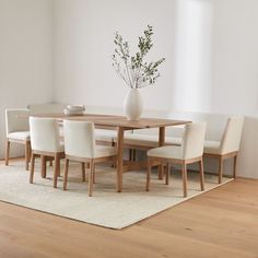 a dining room table with white chairs and a vase