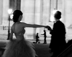 black and white photograph of a woman in a ball gown walking down the street with her arm outstretched