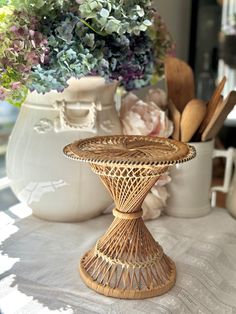 a wicker cake stand sitting on top of a table next to vases with flowers in them