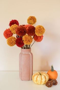 an arrangement of flowers in a vase next to some pumpkins and acorns