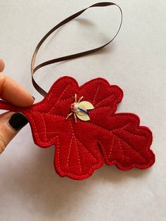 a hand holding a red felt leaf ornament with a gold button on it