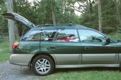 a car with its hood open parked on the side of a road in front of some trees