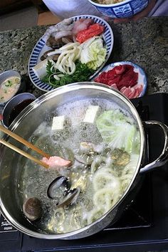 a pot full of soup with chopsticks in it and other dishes on the stove