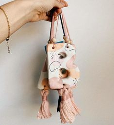 a hand holding a pink and white phone case with tassels hanging from it