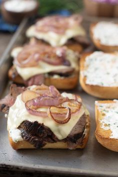 sandwiches with meat and cheese on them sitting on a baking sheet, ready to be eaten