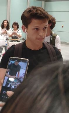 a young man holding up a cell phone in front of his face while standing next to a group of people