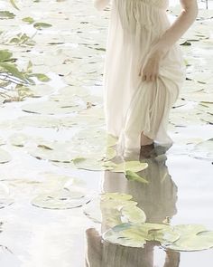 a woman in a white dress is standing in the water with lily pads on her head