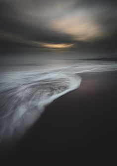 an ocean with waves coming in to the shore and dark clouds above it at night