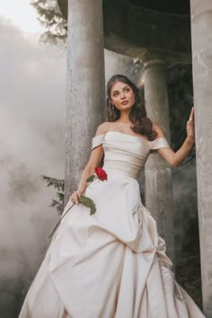 a woman in a white dress standing next to some pillars and holding a red rose