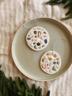 two ceramic ornaments are sitting on a plate next to some pine branches and evergreen needles