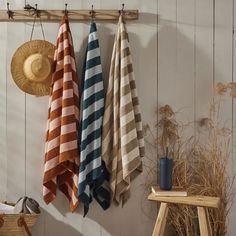 three towels hanging on a wall next to a basket and table with a straw hat