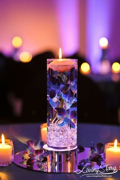 some candles are sitting on a table with flowers and water in the centerpieces