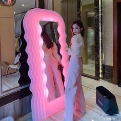 two women are standing in front of a large mirror with the reflection of them on it