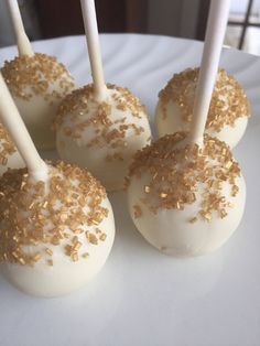 four cake pops with white frosting and gold sprinkles on a plate