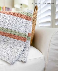 a crocheted blanket sitting on top of a white couch next to a basket