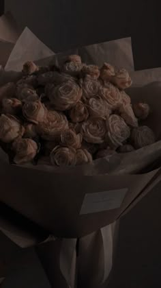 a bouquet of roses wrapped in brown paper on a dark background with the light coming from behind it