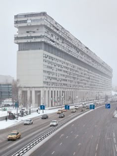 cars are driving down the road in front of a large building on a snowy day