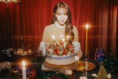 a woman standing in front of a cake with lit candles on it and surrounded by other foods