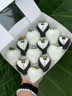 a hand holding a box filled with chocolate covered heart shaped cake treats on top of a green leafy background