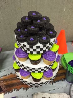 a three tiered cake decorated with purple and green cupcakes