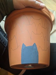 a person holding a clay pot with a blue cat painted on the front and side