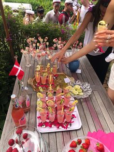 people are standing around a wooden table with drinks and fruit on it, including strawberries