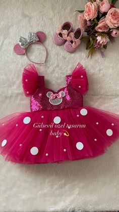 a pink dress with white polka dots and minnie mouse ears is on the floor next to flowers