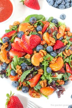 a white plate topped with fruit salad next to blueberries and strawberries