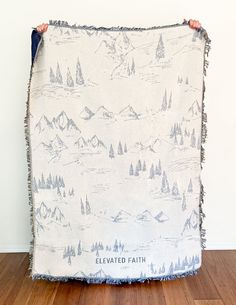 a person holding up a blanket with trees on it in front of a white wall