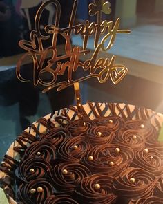 a chocolate cake with the words happy birthday written on it in gold letters and swirls