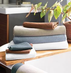 several folded towels are sitting on a wooden shelf next to a potted plant in a bathroom