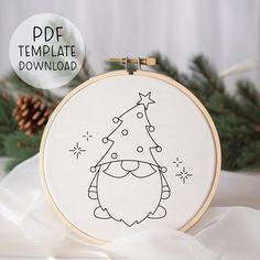 a hand embroidered christmas ornament with a tree on it and pine cones in the background