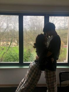 two people standing next to each other in front of a window with the view outside