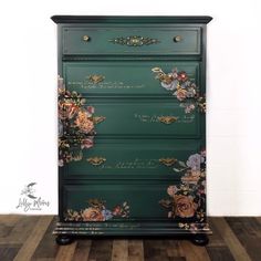 a green dresser with flowers painted on the top and bottom, in front of a white wall