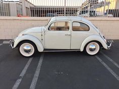 an old vw bug is parked in a parking lot next to a brick wall