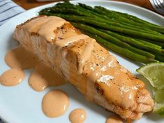 a white plate topped with meat covered in sauce and asparagus next to a fork