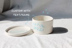 a white ceramic cup and saucer sitting on top of a bed with the words custom with textname below it