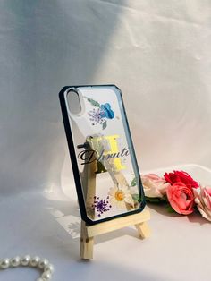 a phone case sitting on top of a table next to flowers and a beaded necklace