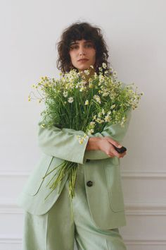 a woman holding flowers in her hands and wearing a green suit with buttons on the front